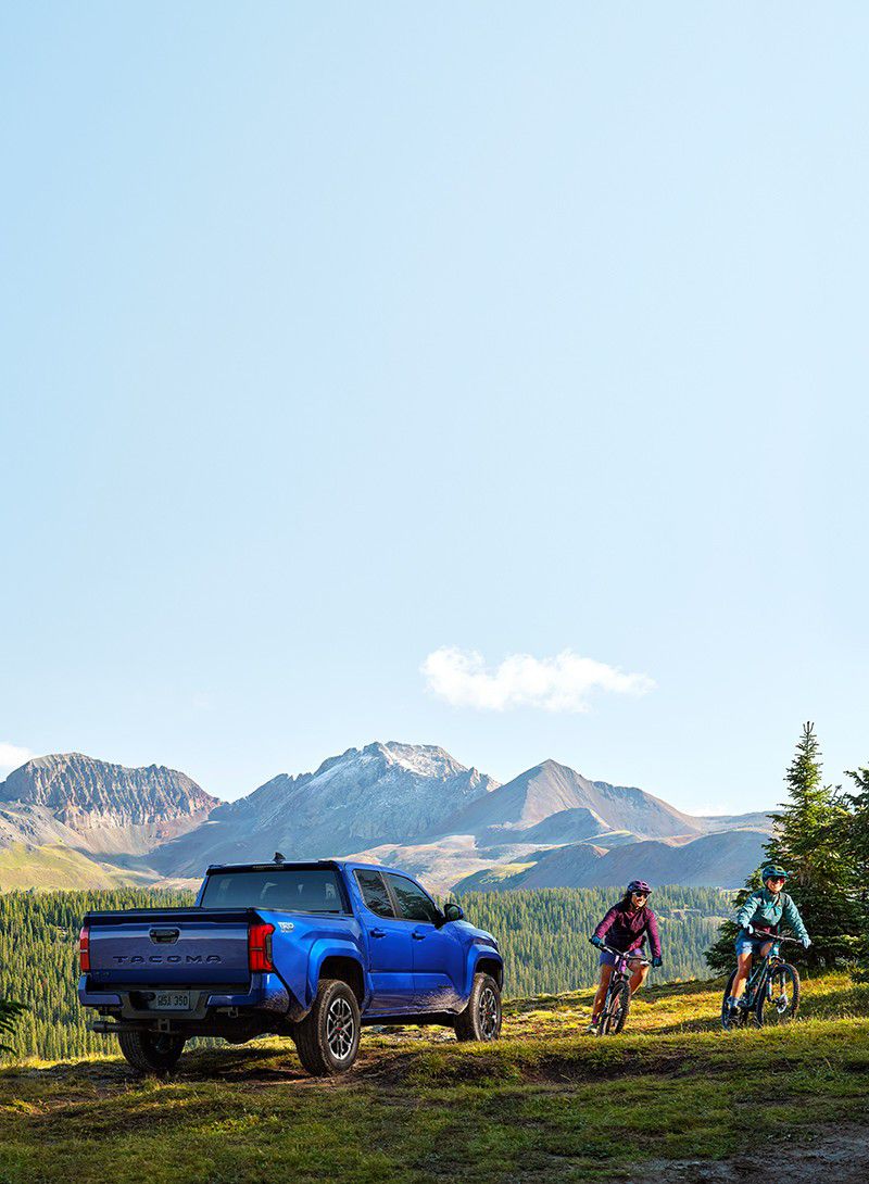 Couple biking next to a blue Toyota truck with mountains in the background.