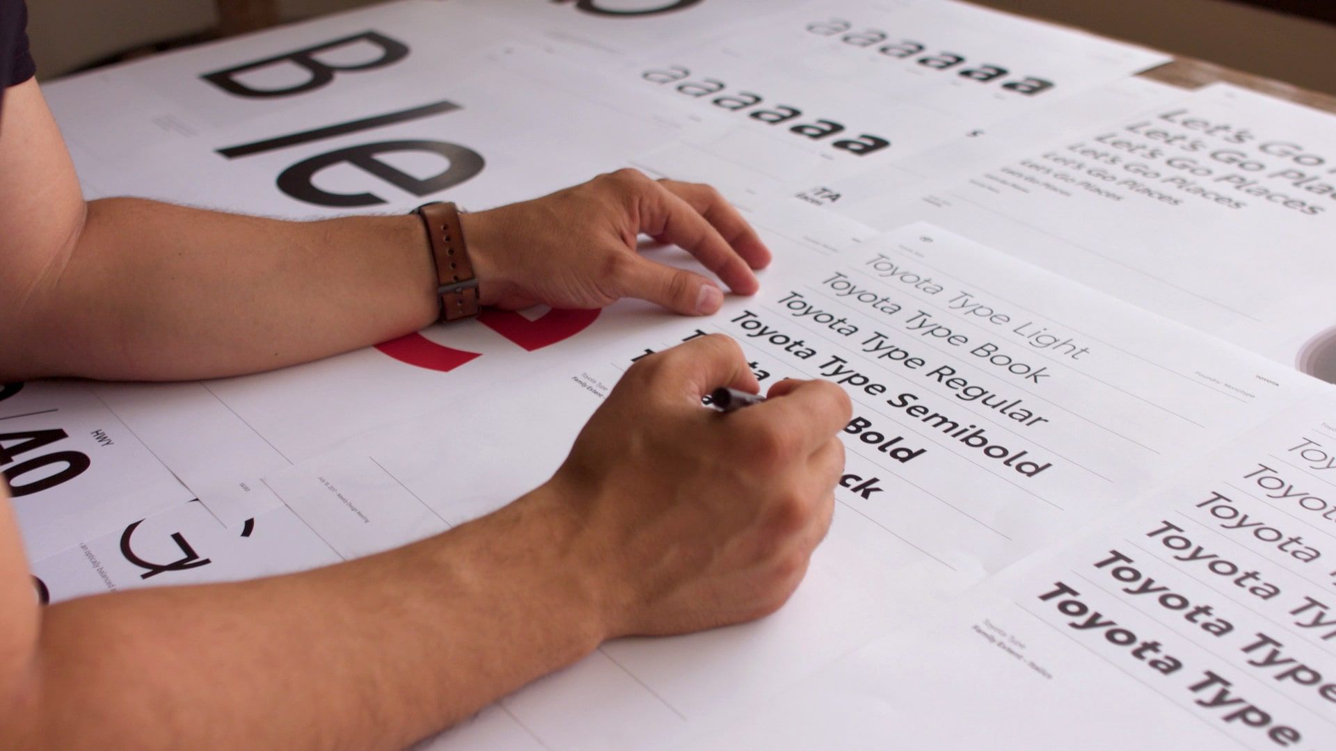 A man’s hands hover over proofs of different Toyota Type font weights.