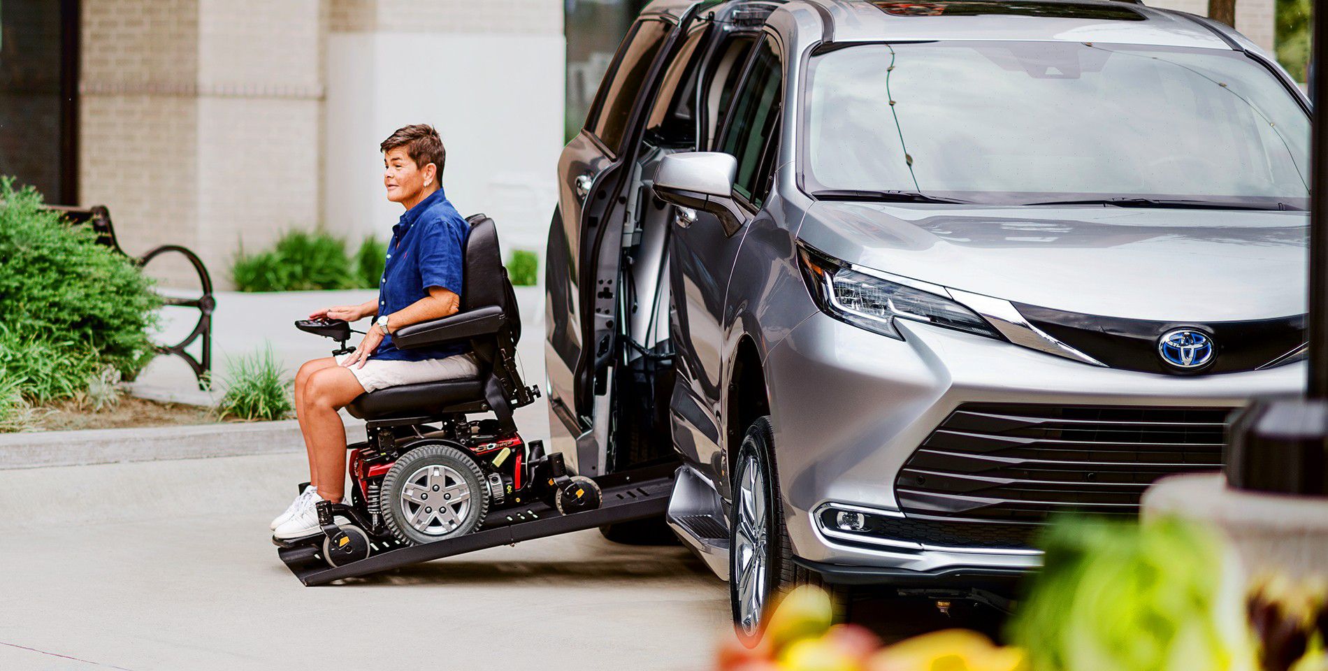 A man in a wheelchair exits a Toyota vehicle using the wheelchair assist ramp.