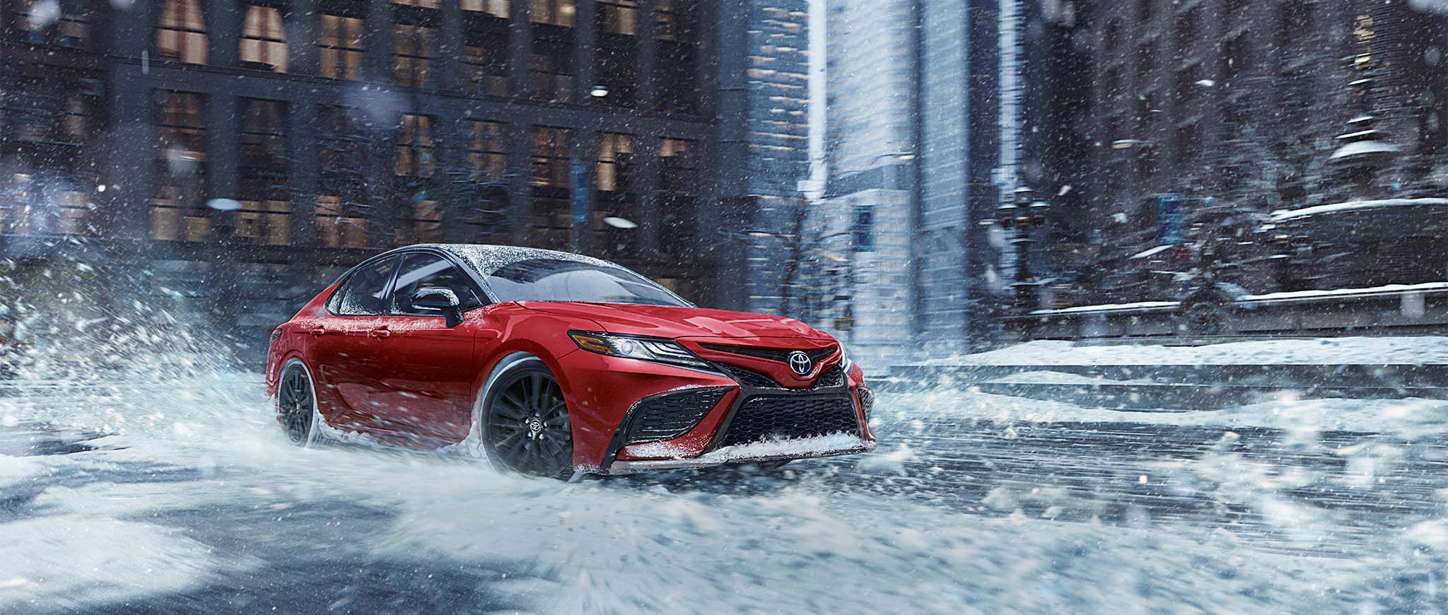 Un Toyota Camry rojo viajando sobre una calle con nieve.