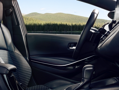 Interior del Toyota Corolla XSE 2023 con una vista de la cima de una montaña boscosa desde la ventana del lado del conductor.