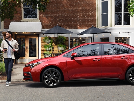 A 2023 Corolla Hybrid in the Color Ruby Flare Pearl is parked at the curb in front of a restaurant.