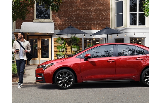 A 2023 Corolla Hybrid in the Color Ruby Flare Pearl is parked at the curb in front of a restaurant.
