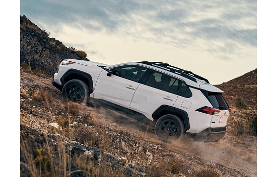 A 2023 Toyota RAV4 in the color Ice Cap kicks up dust as it attempts a hilly climb offroad.