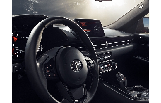 El interior de un Toyota Supra 2023 en negro. En la imagen se muestra el volante, conjunto de indicadores, la palanca de cambios, las perillas y los controles; botones con iluminación de acento LED roja.