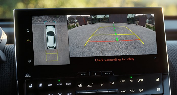 A white Toyota using Intelligent Park Assistant featuring colored gridlines to help the driver park the vehicle in an urban tarred parking lot with houses out front