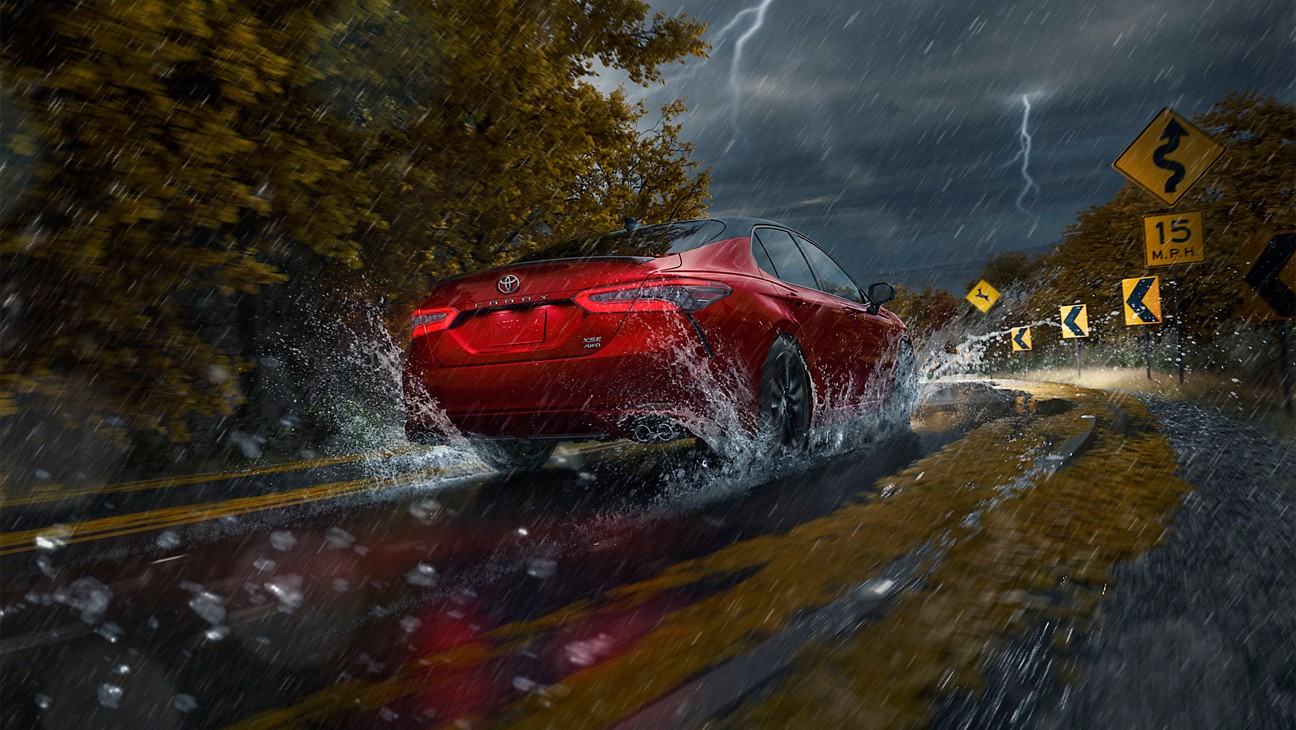 a red car driving on a paved road in a thunder storm