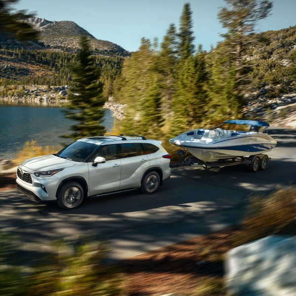 a pearl white suv driving hauling a boat next to a lake