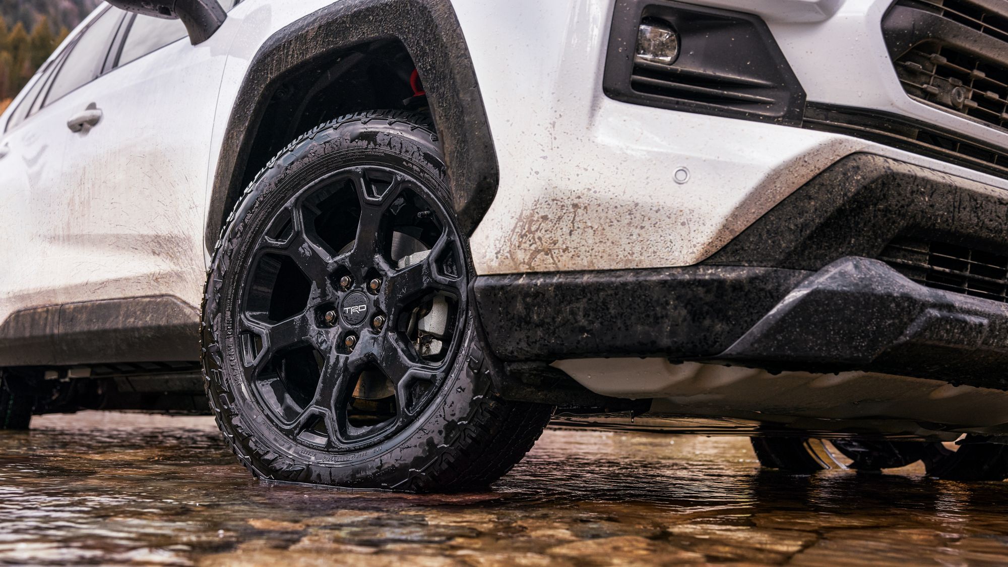 Wet muddy RAV4 front passenger 18 inch 6 spoke matte-black TRD flow-formed alloy wheel with black lug nuts on off road tires