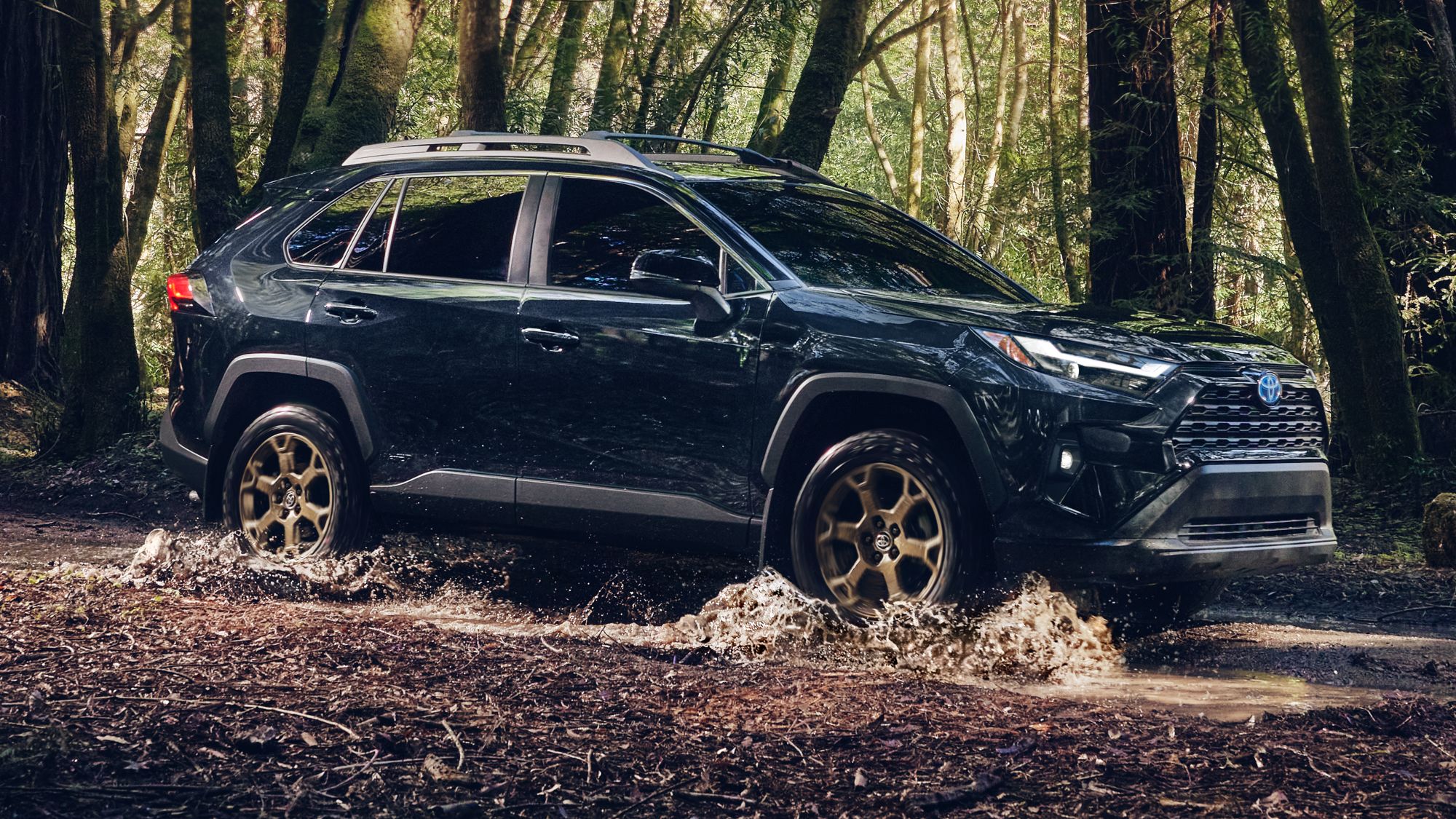 Toyota RAV4 adventure package with bronze wheels and offroading tires threading through muddy water in a forrest