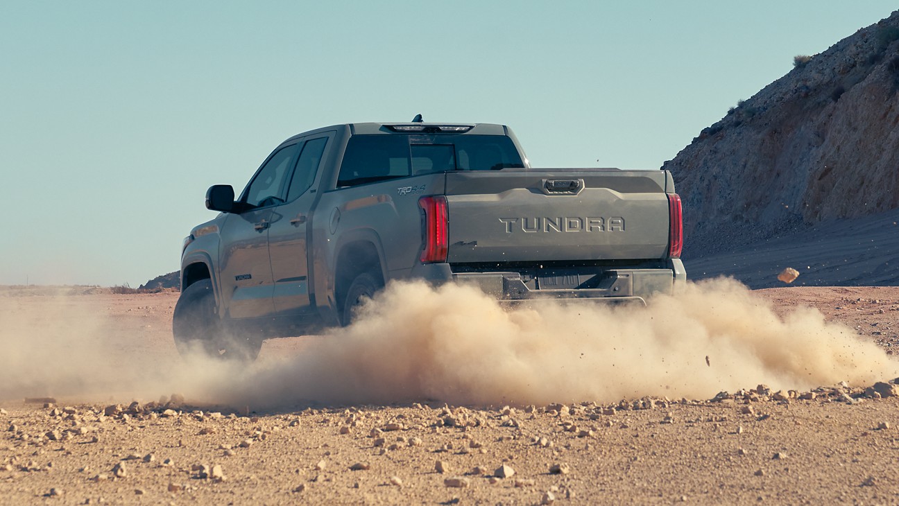 the back of a gray truck driving on dirt in the desert