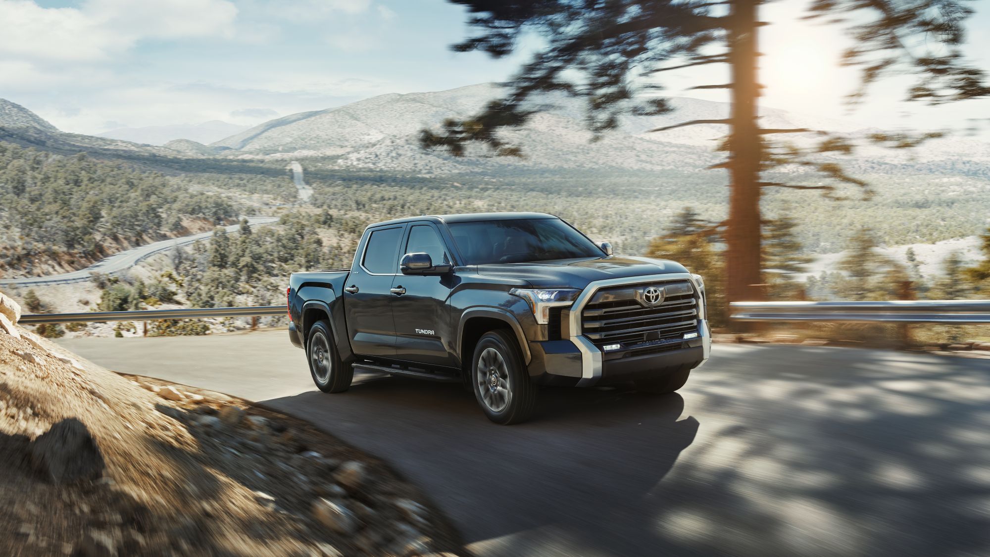 2024 Toyota Limited CrewMax Tacoma shown in Magnetic Gray Metallic driving down a two lane highway under some trees