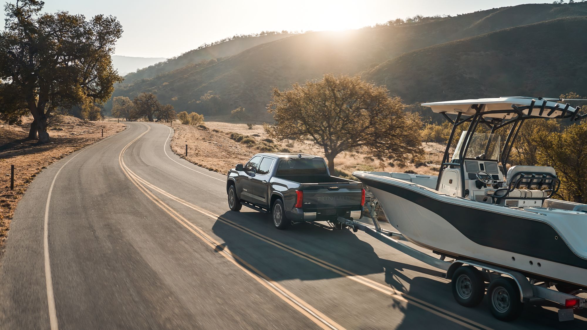 Grey 2024 Toyota Tundra towing a large cruise boat on two lane country highway