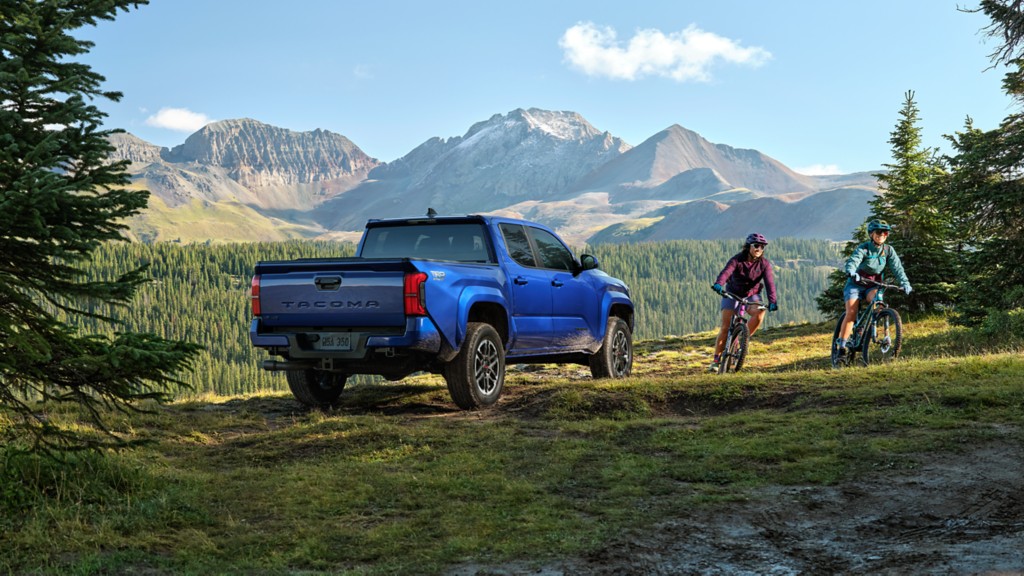 Blue Tacoma parked in the countryside with two bikers riding away