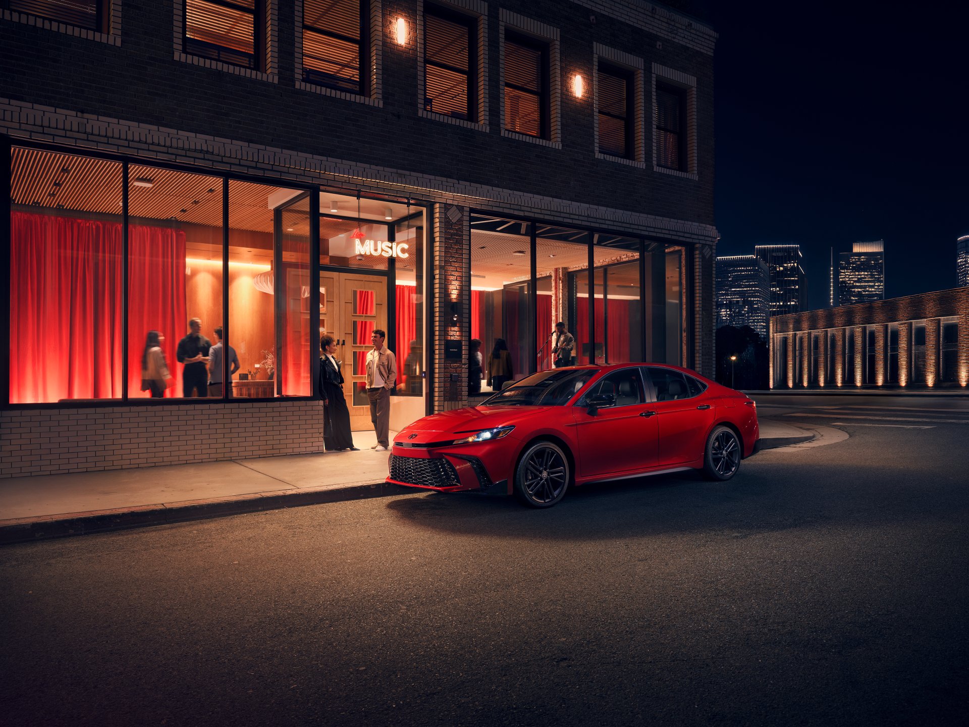 Red 2026 Toyota Camry parked at the curb outside a lit-up music venue