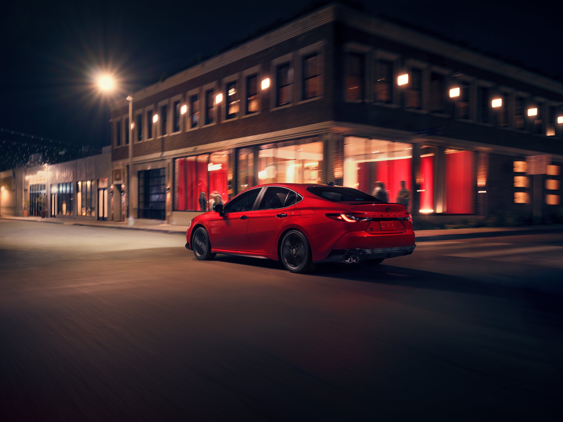 Red 2026 Toyota Camry sedan driving down a city street at night