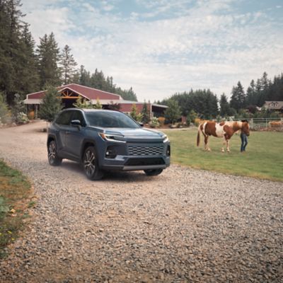 Official Toyota image of a 2026 RAV4 driving on a gravel road past a horse and barn