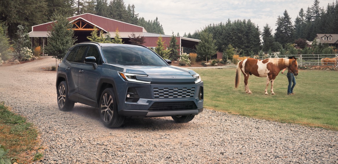 Official Toyota image of a 2026 RAV4 driving on a gravel road past a horse and barn
