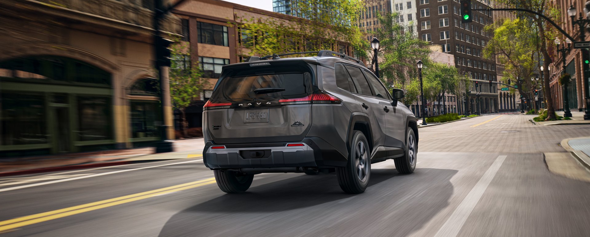 Rear three-quarter view of a gray 2026 Toyota RAV4 Plug-in Hybrid driving on a city street